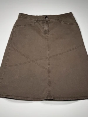 Trussardi Brun a-linjeformad kjol med ficka - Snygg brun kjol i a-linjeform med dekorativa sömmar och en knappstängning fram. Kjolen har en ficka med knapp bak och veckad detalj nedtill. Tillverkad i ett mjukt bomullstyg som ger en avslappnad look. 0071