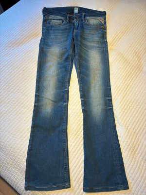 Blå Replay bootcut jeans storlek ’24’ - Snygga Replay blå bootcut jeans med ljusa slitningar framtill och bak. Klassisk femficksmodell med normal midja och dragkedja. Jeansen har en lätt utsvängd passform nedtill och är gjorda i mjukt denimtyg som sitter skönt. Waist 24 length 32