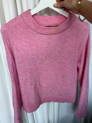 Rosa stickad tröja med rund hals - Mysig rosa stickad tröja med rund halsringning och långa ärmar. Tröjan har en enkel, rak passform och ribbstickade muddar vid ärmslut och nederkant. Perfekt för dig som gillar en söt och avslappnad stil. Defekter syns i bilderna 