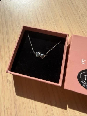 Silverhalsband med hjärtan från Edblad - Säljer ett stilrent silverhalsband från Edblad med två små hjärtan som hänge. Kedjan är tunn och elegant, och halsbandet kommer i original ask. Perfekt accessoar för att lyfta vilken outfit som helst.
