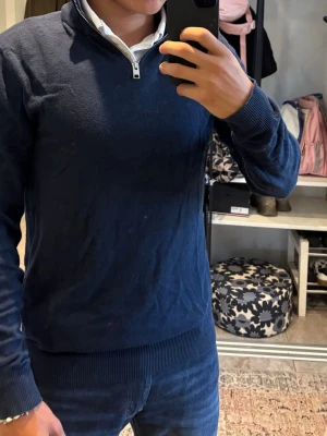 Mörkblå halvzip tröja - Mörkblå stickad tröja från Jack & Jones med halvzip och ribbade muddar vid ärmslut och nederkant. Tröjan har en klassisk passform och är perfekt att bära över en skjorta för en clean och stilren look. Tröjan har storlek XS men funkar även till S.