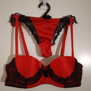 Elegant feminint BH set med spets från H&M. Röd, svart. 75A, 36. - Elegant set med BH+byxa från H&M med svarta spetsdetaljer och justerbara axelband. Materialet är en mix av polyamid, polyester och elastan som ger en mjuk och följsam känsla, satin. BH'n har en feminin form och en liten rosett framtill för extra stil. Strlk 75A, Byxa 36. Felfritt. Byxa oanvänd. Passar perfekt till tex jul. Se bilder för egen bedömning.
