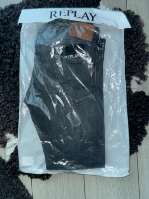 Mörkgråa Replay jeans med bakficka - Helt nya Snygga gråa jeans från Replay med klassisk femficksdesign och diskret broderad detalj på bakfickan. Jeansen har en rak passform och är tillverkade i ett mjukt denimtyg som ger en skön känsla. Perfekta för dig som gillar stilrena och tidlösa plagg. Säljs eftersom plagget ej passade just mig men fungerar för en person mellan 170-80 och är en slim fit modell