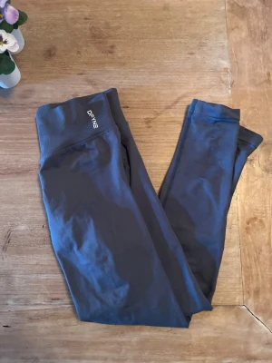 DFYNE träningsbyxor  - Snygga mörkgrå leggings från DFYNE. Tight passform och stretchigt material som sitter skönt. Perfekta till träning eller chill. Diskret logga framtill på linningen.