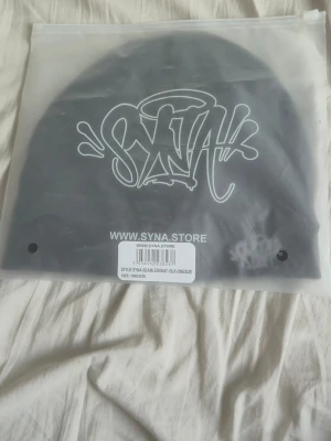 Svart mössa från SYNA STORE - Snygg svart mössa från SYNA STORE med broderad logga i vitt framtill. Mössan är enkel och stilren med en tight passform och tillverkad i mjukt material. Perfekt för dig som gillar streetwear och vill ha en clean look.
