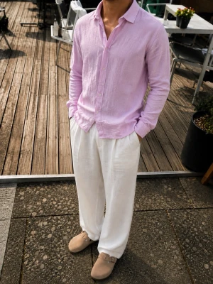 Riley Slim Fit Linne Skjorta – Ljusrosa – Strl M - Snygg och stilren skjorta från Riley, modell Slim Fit, i en ljusrosa/lila nyans. Tillverkad i 100 % linne, vilket gör den perfekt för sommaren – sval, luftig och med en naturligt avslappnad look.  Skjortan har klassisk krage, pärlemorskimrande knappar och en stilren design. Använd den både till vardags och till en mer uppklädd outfit. Passar riktigt bra tillsammans med ljusa linnebyxor och loafers/tofflor.  Storlek: M Material: 100 % linne Färg: Ljusrosa / pastellrosa Passform: Slim Fit