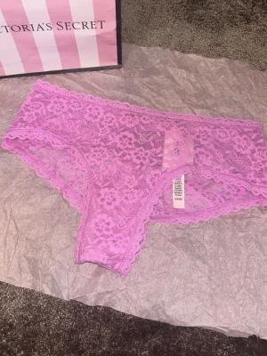 Ljuslila spets-trosa från Victoria's Secret - Supersöt ljuslila trosa i spets från Victoria's Secret. Modellen har breda kanter och ett blommigt spetsmönster som ger en romantisk vibe. Perfekt för dig som gillar feminina detaljer och mjuka material.