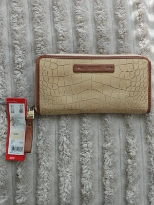 Beige plånbok med krokopräglat mönster - Beige plånbok från Esprit med krokopräglat mönster och bruna detaljer. Plånboken har dragkedja runtom och en avtagbar handledsrem. .