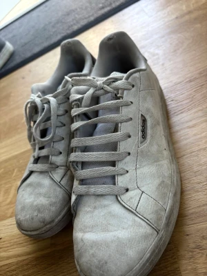 Vita Adidas sneakers med svart detalj - Säljer ett par klassiska vita Adidas sneakers med lågt skaft och svart detalj på hälen. Skorna har en enkel och stilren design med snörning och diskret Adidas-logga på sidan. Tillverkade i syntetmaterial och textil för en bekväm känsla.