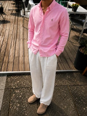 Polo Ralph Lauren Rosa Skjorta – Slim Fit – Herr M - Snygg Polo Ralph Lauren skjorta i en ljusrosa färg med klassiskt broderat Polo Pony-emblem på bröstet. Skjortan är i Slim Fit och har button-down-krage samt klassisk knappstängning.  ✨ Märke: Polo Ralph Lauren 🎨 Färg: Ljusrosa 📏 Storlek: M 👔 Passform: Slim Fit 🧵 Detaljer: Broderad Polo Pony-logga, button-down-krage  Skjortan har en snygg, lätt strukturerad väv och passar perfekt till både vita linnebyxor, chinos eller jeans. Perfekt för en stilren och somrig outfit.