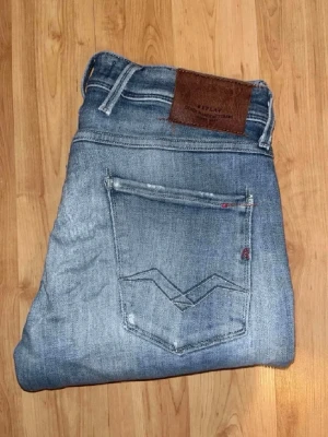 Replay jeans  - Ljusblåa Replay jeans med slitningar och hål med en slim passform. Midja 38cm, längd 110cm. Obs jeansens tyg baktill har blivit något förtunnat - se bild. JAG SKICKAR EJ FLER BILDER NÄR JAG BÄR JEANSEN! för bättre inblick i passformen rekommenderar jag att googla på modellnamnet. För storleksguide kolla måtten noggrant då jeansen alltid kan vara uppsydda heller krympta och jag ej tar emot returer :) (r12)