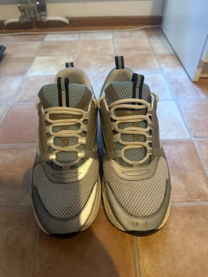 Grå chunky sneakers med blå detaljer - Säljer ett par chunky sneakers i grått med blå och svarta detaljer. Skorna har meshpaneler för extra ventilation, vita snören och en tjock vit sula. Perfekta för dig som gillar en sportig och trendig look.