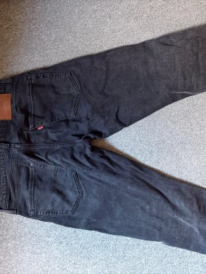 Svarta raka jeans med fem fickor - Säljer ett par svarta jeans med klassisk femficksmodell och raka ben. Jeansen har en läderpatch bak i midjan och detaljer i metall. Materialet är denim i bomull och passformen är avslappnad. Perfekta för en cool och enkel stil. Modell 502