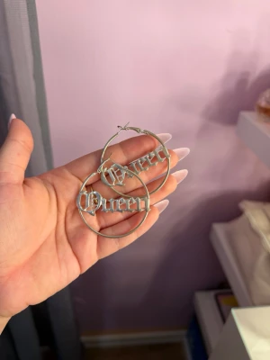 Silvriga hoop örhängen med Queen-text - Silvriga hoop-örhängen med texten ”Queen” 🤍✨ Klassiska och stilrena örhängen i silverfärg som ger extremt mycket baddie vibes 😍Passar perfekt till både vardag och fest och är enkla att matcha med andra smycken. Fint skick!