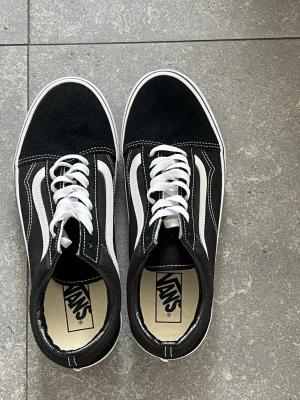 Svarta Vans Old Skool sneakers - Klassiska Vans Old Skool sneakers i svart mocka och canvas med vita detaljer och vit sula. Skorna har den ikoniska vita sidan, vita skosnören och kontrastsömmar. Perfekta för en streetwear-look och passar till det mesta. Använda 1-2 gånger så literally nya! Säljer dem för 400 kr men kan möjligtvis gå med på priser ner till 300 kr!