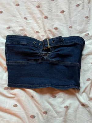 Mörkblå denim tubtopp med bälte - Mörkblå tubtopp i denim med snyggt bälte och metallspänne framtill. Har använt en gång. Är osäker vart den är ifrån men gissar på Cider:)