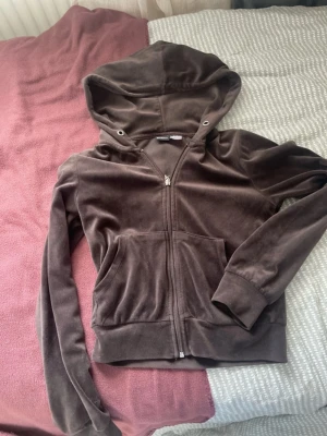 Brun velourhoodie från Gina Tricot - Mjuk och skön brun hoodie i velour från Gina Tricot. Tröjan har dragkedja framtill, två fickor och en stor huva med snörning. Perfekt för en avslappnad och trendig look. Materialet är glansigt och ger en lyxig känsla.