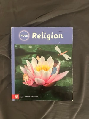 PULS Religion Grundbok - Kursbok i religion med blått och grönt omslag, illustration av näckros och barn samt en trollslända. Boken täcker olika religioner som kristendom, islam, judendom, hinduism och buddhism. Skriven av Marianne Abrahamsson och utgiven av Natur & Kultur.