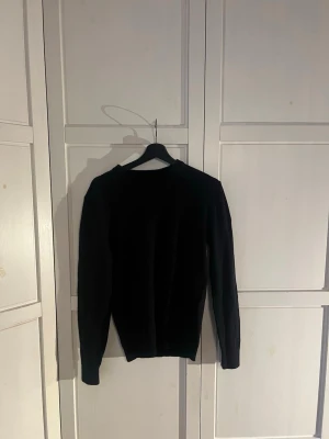 Svart merinoulltröja These Glory Days - Klassisk svart stickad tröja från These Glory Days i mjuk och exklusiv merinoull. Tröjan har rund halsringning, långa ärmar och en clean, minimalistisk look som passar perfekt till alla outfits.
