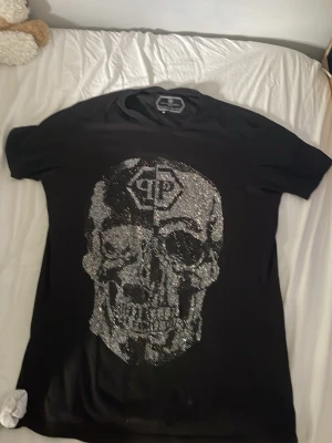 Svart t-shirt med glittrig döskalle - Säljer en svart t-shirt med korta ärmar och en stor glittrig döskalle framtill. Trycket är detaljerat och täckt av paljetter som ger en riktigt cool effekt. Perfekt för dig som vill sticka ut med din stil.            Säljer pga för stor de är M men passar 100 procent någon som har L 