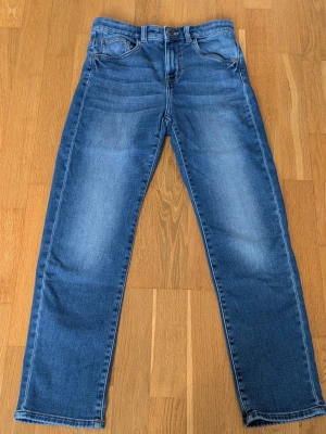 Blå raka jeans från KappAhl - Säljer ett par klassiska blå jeans med raka ben. Jeansen har fem fickor, bälteshällor och knappgylf. Materialet är denim i bomull med snygg tvättad look. Perfekta till en avslappnad stil.