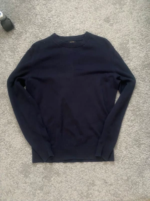 Mörkblå stickad tröja Massimo Dutti - Mörkblå stickad tröja från Massimo Dutti i en mjuk blandning av bomull och ull. Tröjan har rund halsringning, långa ärmar och ribbade muddar vid hals, ärmslut och nederkant. Enkel och stilren design som passar till det mesta.
