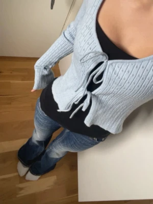 Ljusblå ribbad kofta med knyt - Supersöt ljusblå kofta med ribbad struktur och två knyt framtill. Koftan har lång ärm och djup v-ringning, perfekt att slänga över ett linne eller topp. Materialet är mjukt och stretchigt, vilket gör den riktigt bekväm.
