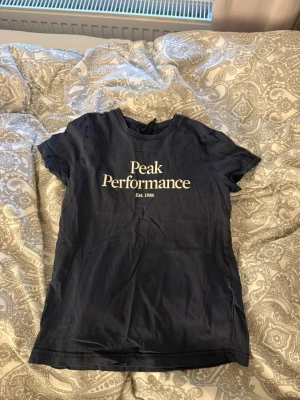 Mörkblå Peak Performance t-shirt - Snygg mörkblå t-shirt från Peak Performance med vit logga och text 'Est. 1986' på bröstet. Klassisk rund hals och korta ärmar. Perfekt till jeans eller shorts för en clean och sportig look.