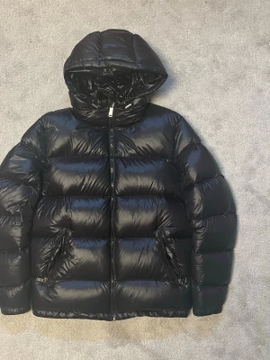 Zara dunjacka  - Säljer en snygg Zara dunjacka i svart. Varm och rejäl modell med blank finish, huva och två fickor med dragkedja.  • Storlek: S • Färg: Svart • I princip nyskick • Använd väldigt lite • Huva med justerbara snören • Två fickor med dragkedja • Dragkedja framtill • Stilren och varm modell