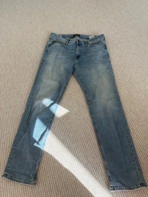 Ljusblå jeans från Jack & Jones - Säljer ett par ljusblå jeans från Jack & Jones med klassisk femficksmodell och regular fit. Jeansen har en snygg tvättad look och raka ben. Perfekta för en avslappnad stil och passar till det mesta i garderoben.
