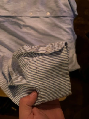 Blåvit randig skjorta med knappar - Snygg skjorta med tunna blå och vita ränder. Klassisk krage och långa ärmar med manschett och knapp. Skjortan har en avslappnad passform och är tillverkad i ett mjukt bomullstyg. Perfekt för en clean och stilren look.