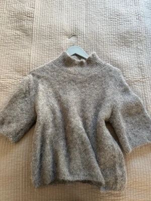 Beige stickad tröja Gina Tricot - Mysig beige stickad tröja från Gina Tricot i alpackablandning. Tröjan har korta ärmar, hög krage och en fluffig, mjuk känsla. Perfekt för lager på lager och en avslappnad men trendig look. Nästan helt ny då jag använt den ett fåtal gånger. 