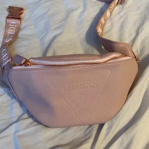 En magväska i märket GUESS - En rosa magväska i märket GUESS. Man kan minska väskan och man kan göra den större vid midjan 