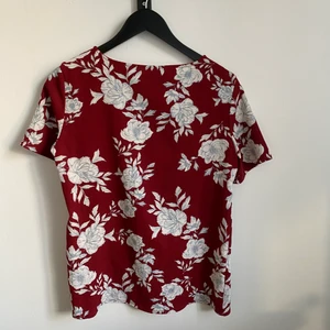 Röd t-shirt med blommor - Vinröd t-shirt med blåvita blommor. 96 % polyester. 