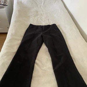 Kostymbyxor från Gina  - Svarta kostymbyxor med liten ”söm”/”ridge” på framsidan. Knapp och dragkedja vid sidan. Smalare åt lår och rumpa, vidare nertill ✨