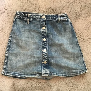 Kort jeanskjol  - En kort, blå jeanskjol med 5 knappar, varav 2 av dom kan användas. Kjolen är använd ett fåtal gånger. Säljer denna pågrund av att den är för liten på mig.