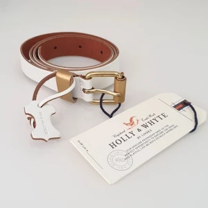 vitt skärp läder 75 Lindex Holly & Whyte - Färg: vitt.  Strl: 75.   Mått:  Total längd: 90 cm.  Bredd: 2,5 cm.  Till första hål & sista hål: 72 cm - 84,5 cm.   Helt nytt skärp från Lindex, Holly & Whyte. Vitt med gulddetaljer. Läder. (Real Leather) Med prislapp/tags kvar. Betalning via swish, frakt tillkommer.