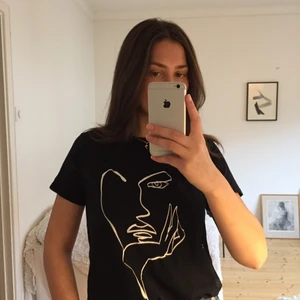Svart t-shirt med vitt tryck - En svart t-shirt med ett vitt tryck föreställande konturerna av ett ansikte. Använd fåtal gånger.