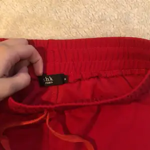Ett par röda byxor med rak modell som man kan knäppa upp längst med kanterna 