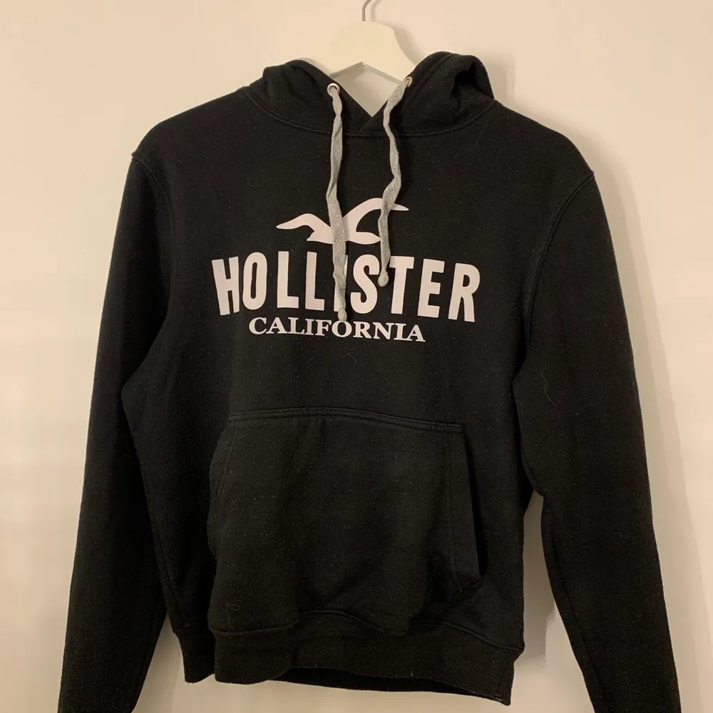 En svart hoodie med vitt tryck från Hollister i storlek XS.. Hoodies.