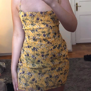 Gul blommig sommarklänning  - Gul blommig sommarklänning med snörning på ryggen. Blommönstret är mörkblått. Endast provad annars är den som ny