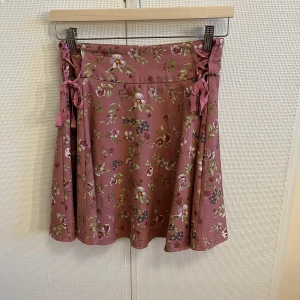 Blommig kjol  - Jätte söt kjol som tyvärr är lite för lång för mig enligt min smak, den är ganska använd och snörningarna på sidorna är lite slitna men ändå jättefin kjol, vill ni ha fler bilder så skriv. Köparen står för frakt 