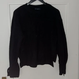 Svart stickad tröja med slits - Mysig stickad tröja från Zara som har knytningar runt handlederna och slitsar i bägge sidor. Säljs för att den inte längre kommer till användning. 