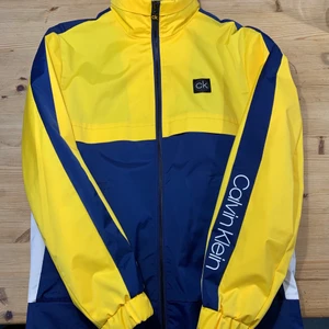 Calvin Klein jacka gul/blå - Sjysst vindtät jacka från Calvin Klein i storlek M. Riktigt fräsch och nästan helt oanvänd utan skador eller slitage.