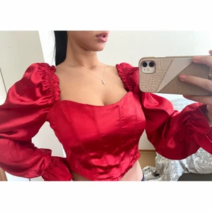 Röd långärmad korsettopp i satin, Strl 34 - En röd satin korsettopp med öppen rygg. Helt oanvänd med bra kvalité samt dragkedja där bak. Storlek 34. Pris kan diskuteras. 