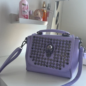 Ljus lila axelväska - Jag säljer en ljuslila axelväska med små dödskallar på, fick den av min moster för 3 år sedan men har aldrig andvänt den.