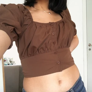 En topp från NA-KD - En jätte fin brun topp med puffiga ärmar från NA-KD! I storlek 34 och i topp skick! Passar bäst för dig som har  B kupa eller lite mer. Jag personligen har A-kupa och de finns mycket mellanrum mellan bh och toppen. Så pass formen kanske inte är den bästa för mindre. Så söt och snygg färg! 