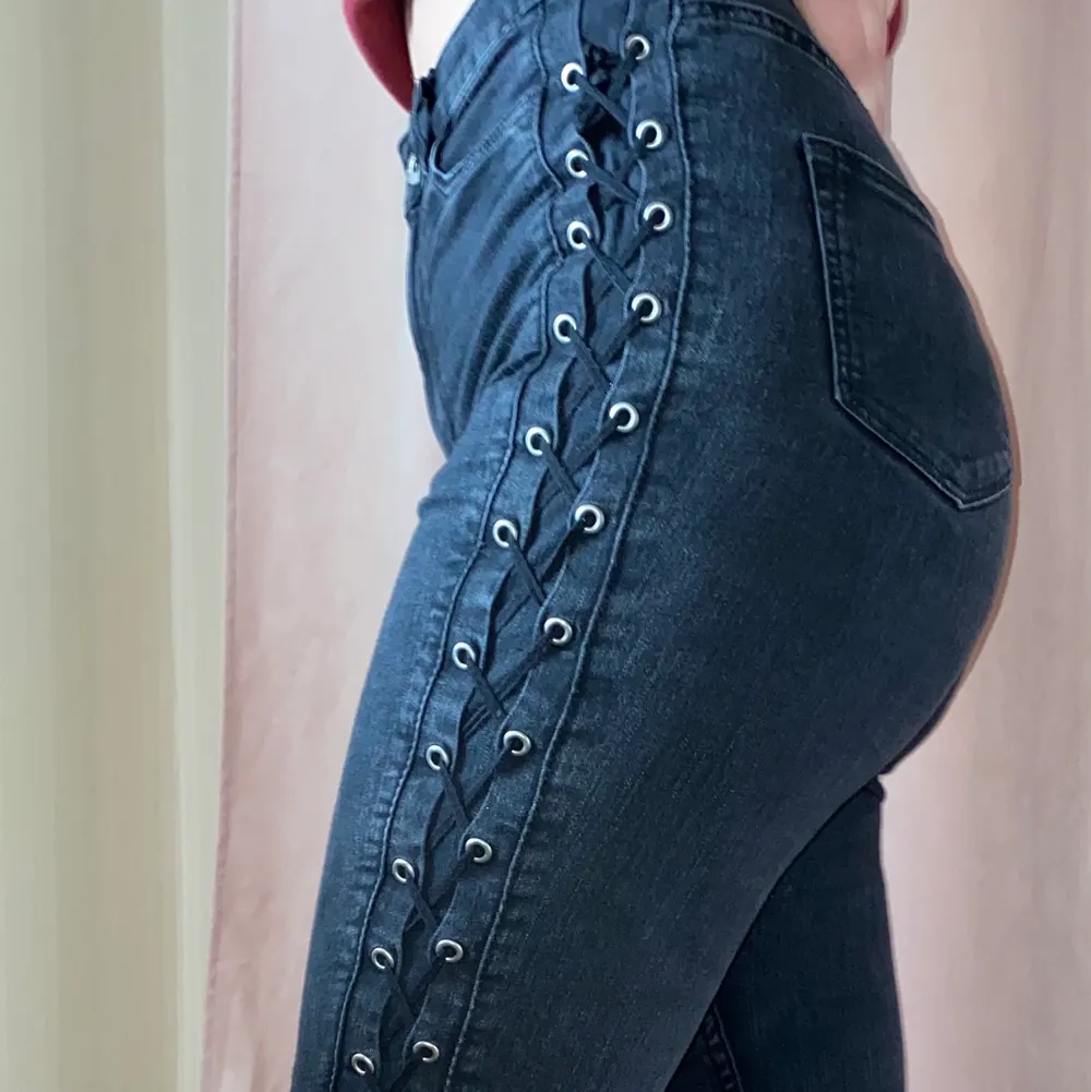 Grå svarta jeans med korsad snörning längs med sidorna av benen och höfterna, storlek 34. Jeans & Byxor.