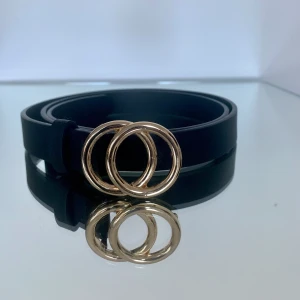 Svart läderskärp från Pieces/ stl: 95/ oanvänt/ höjd: 2 cm.  - Oanvänt skärp från Pieces i storlek 95. Höjd på skärpet är 2 cm. Svart med guldspänne. Går att göra hål i skärpet för annan storlek. Säljes då jag rensar i garderoben. Skriv vid frågor :) 