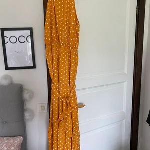 Lång klänning  - Lång orange/gul klänning med vita prickar från Shein. Jag är 164 och klänningen är ner till ankeln på mig. Skön kvalitet. Knytdetalj i midjan som går att reglerna hur man vill. Aldrig använd. Säljer då jag fick en liknande klänning i present.